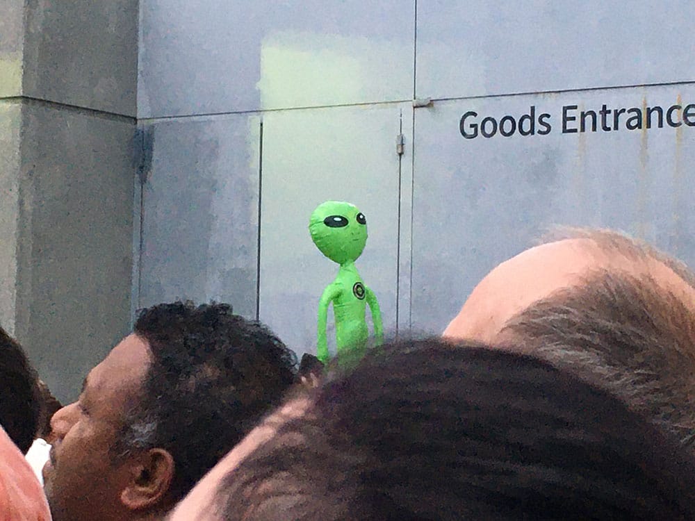 Photo of an inflatable green alien in amongst a sea of heads (some balding)