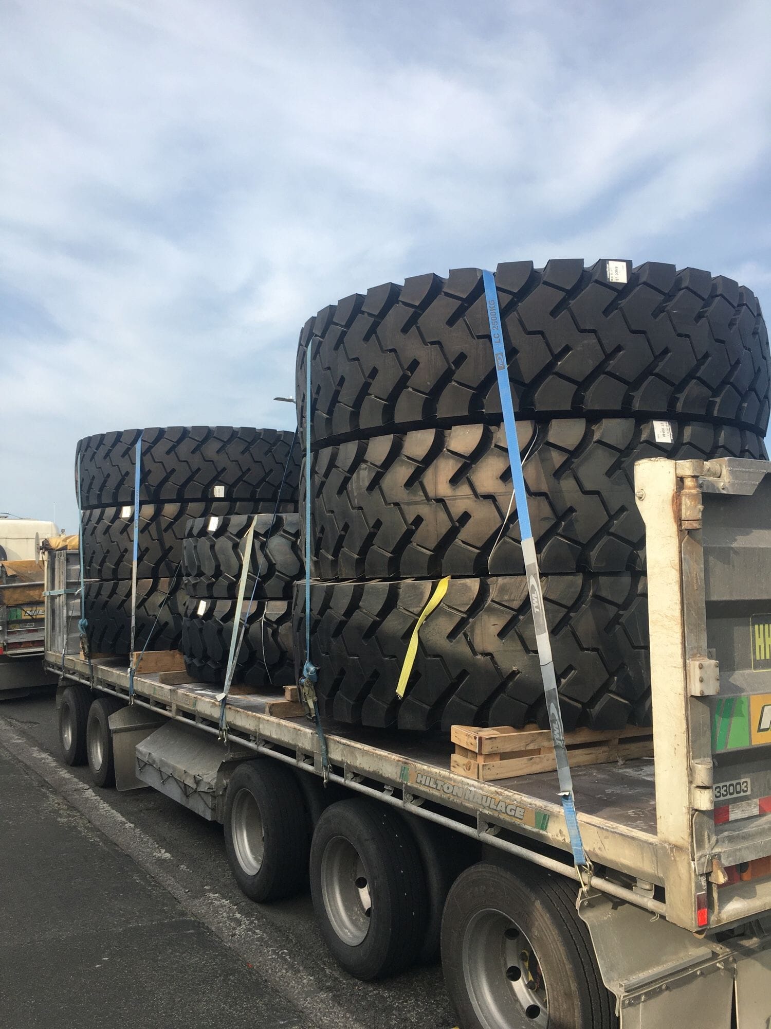 Photo of a truck and trailer. Strapped on the back of the trailer are 8 absolutely enormous tires.