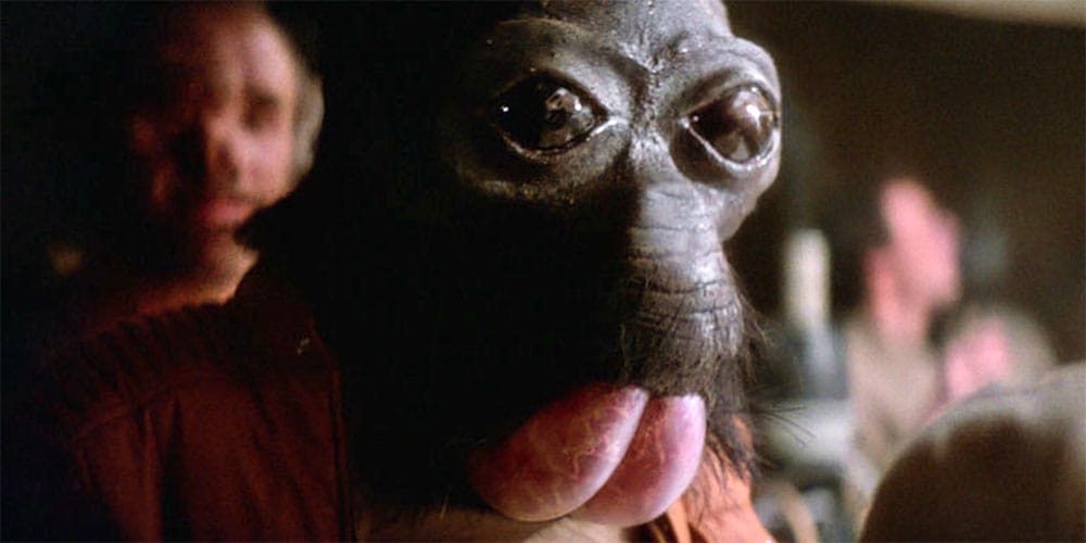 Screengrab of the cantina scene from Star Wars A New Hope showing Ponda Baba, a black skinned alien with large eyes, no nose, and coarse hair around a mouth that looks like a big pink bum.