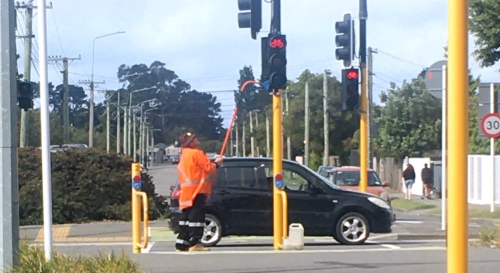 A worker in high-viz using long tool with a curve and blue brush on the end. The approx 1.5m handle is red.