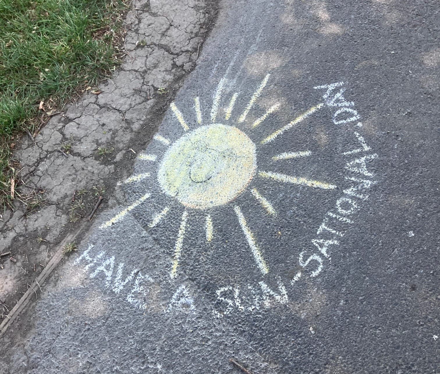 A yellow chalk sun with a smiling face with the words "Have a sun-sational day".