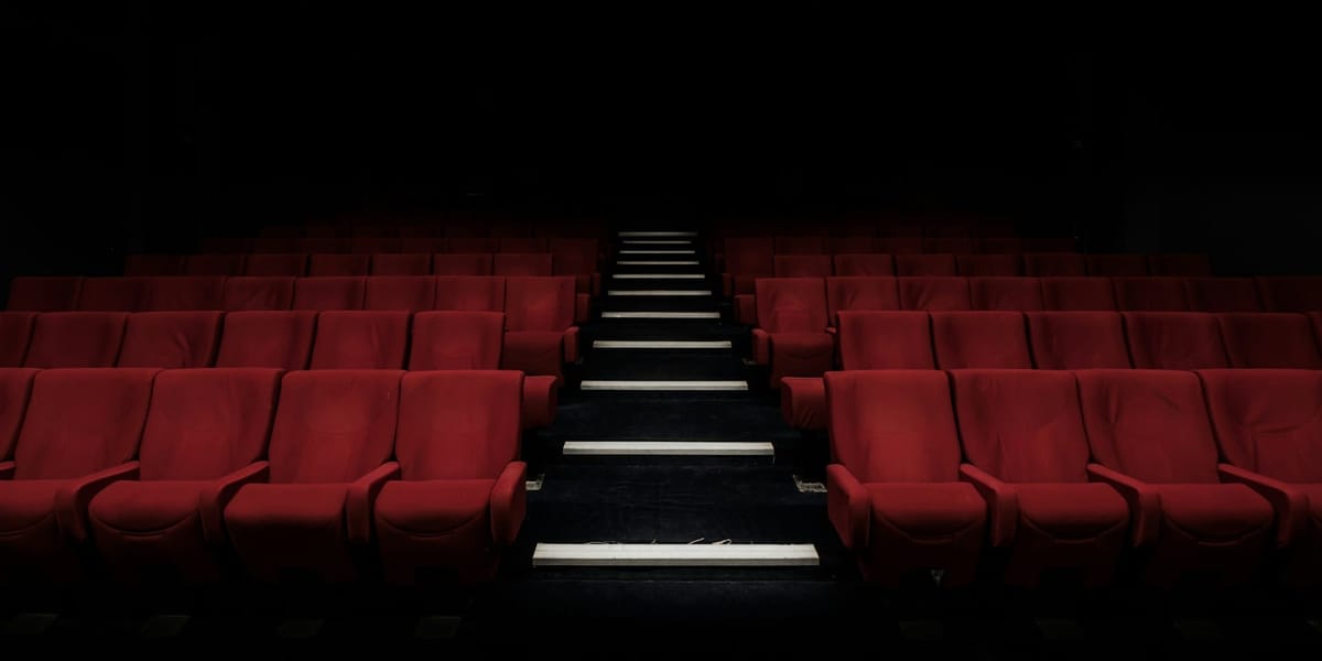 A movie theatre looking at rows of red seats with an aisle running through the middle. They are all empty.
