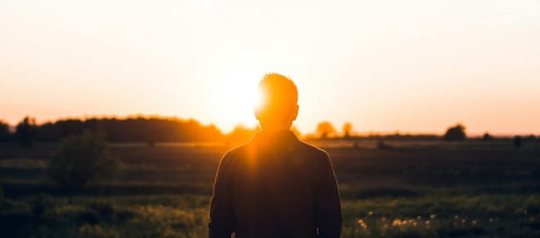 Photo of a young man in silhouette in front of a setting sun.