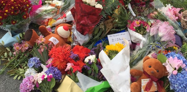 A close up shot of bouquets of flowers, notes and soft toys bundled together on the road. 