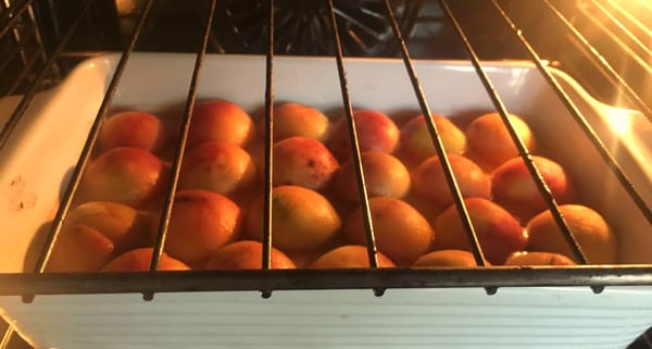 Photo of the inside of an oven and a baking dish of halved peaches roasting.