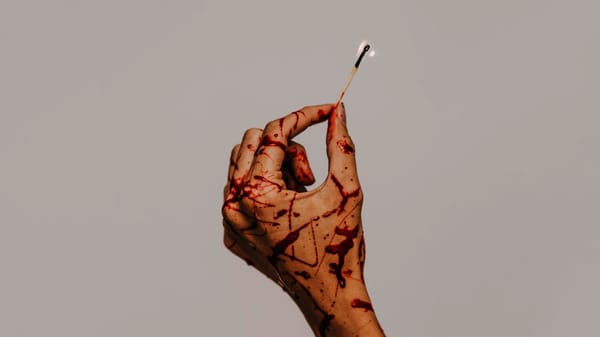 A woman's hand splattered with blood holds a lit match.